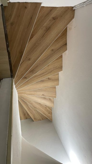 Holztreppe mit spiralförmigen Stufen, die nach unten führen, in hellem Raum.